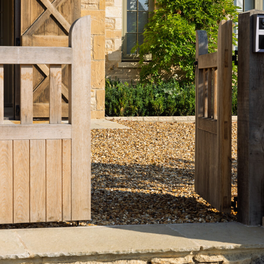 Open oak gate onto a gravel driveway with stone step edging