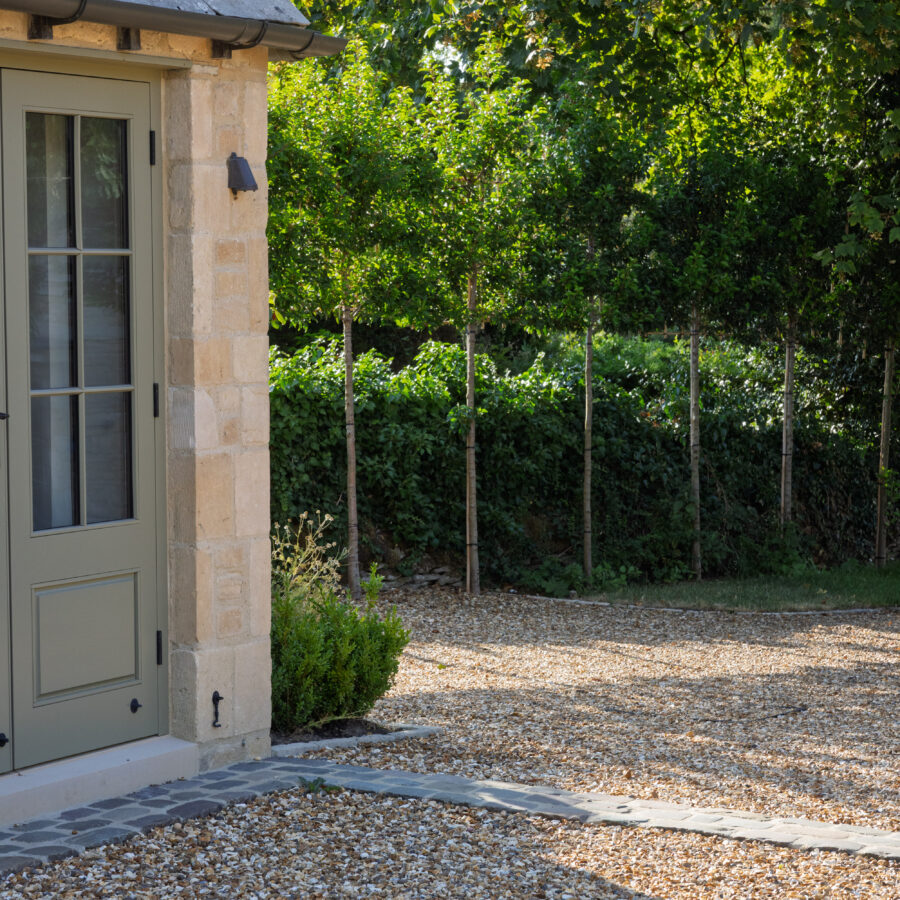 Close detailing of the gravel edge at an outbuilding threshold, driveway sloping down behind